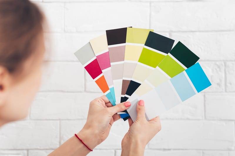 A woman displaying a paint swatch with various colors.