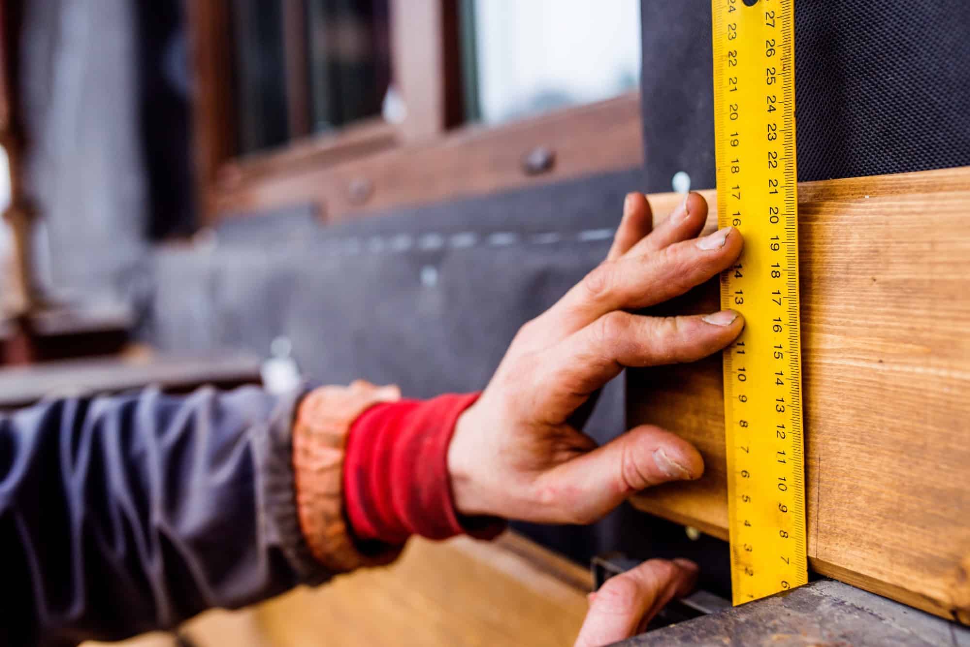 Hand of unrecognizable worker, doing facade, measuring wooden bo