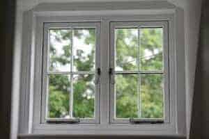 A white window with R7 handles & stays in a room with trees in the background.